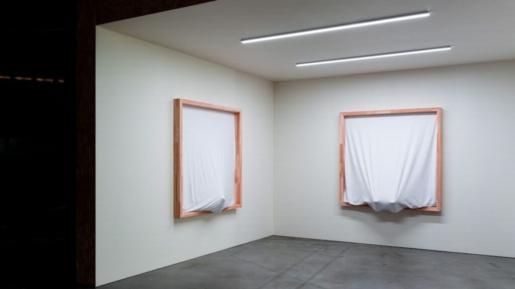 Galleria minimalista con due finestre coperte da teli bianchi